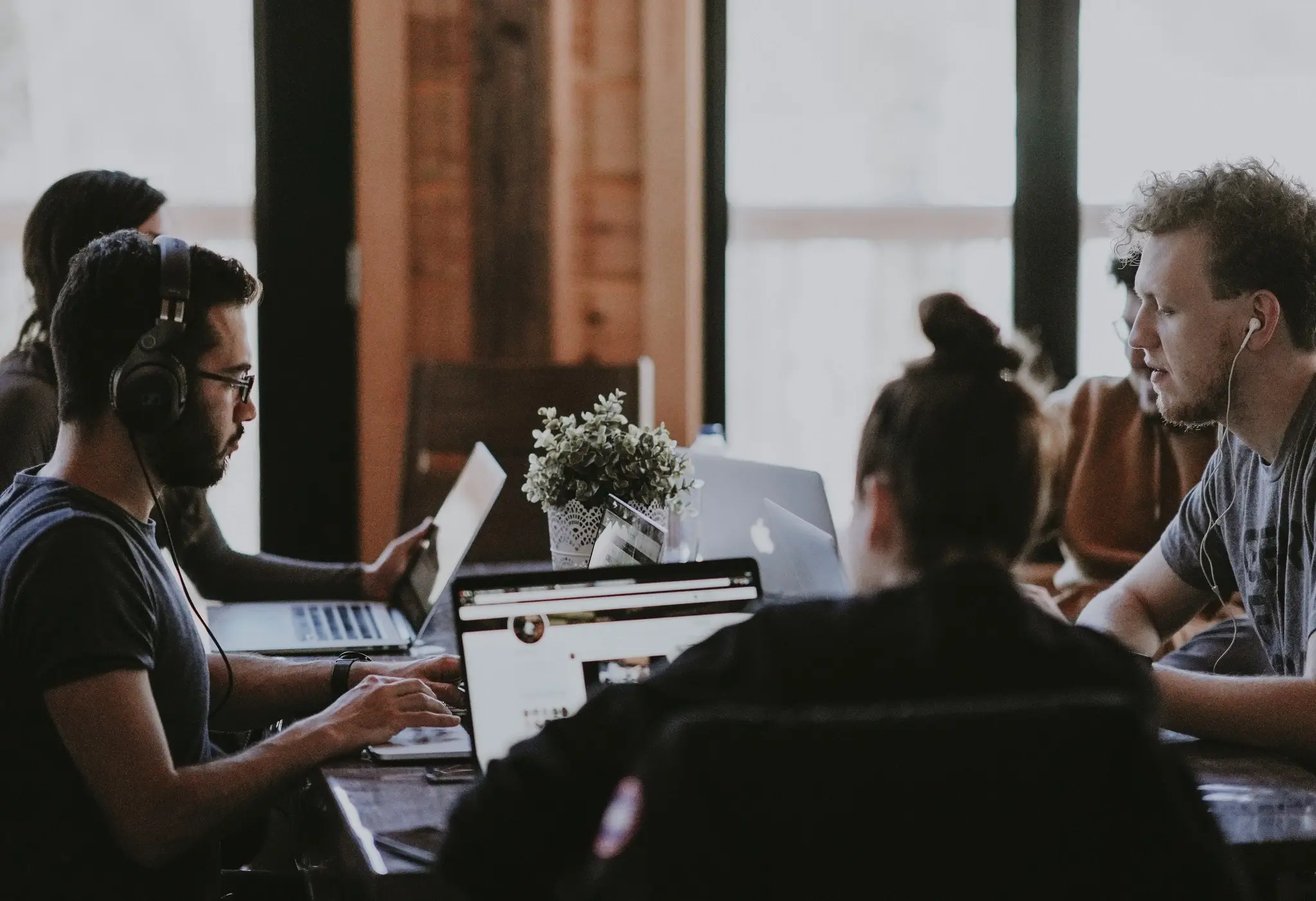 Grupo de jóvenes profesionales colaborando en un espacio de trabajo compartido, utilizando portátiles y concentrados en sus proyectos, simbolizando trabajo en equipo y creatividad.