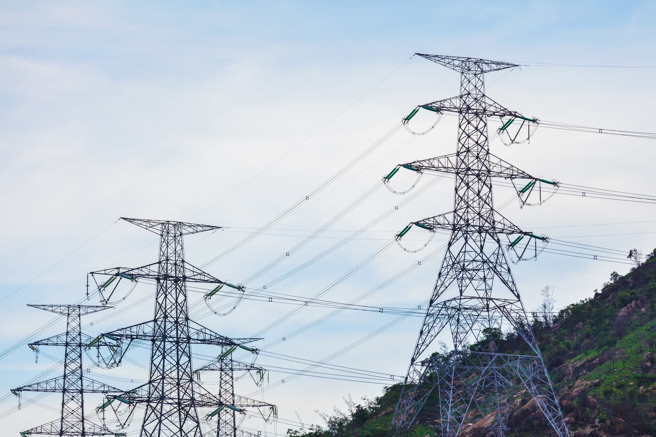 Torres de alta tensión con cables de energía eléctrica contra un cielo azul.