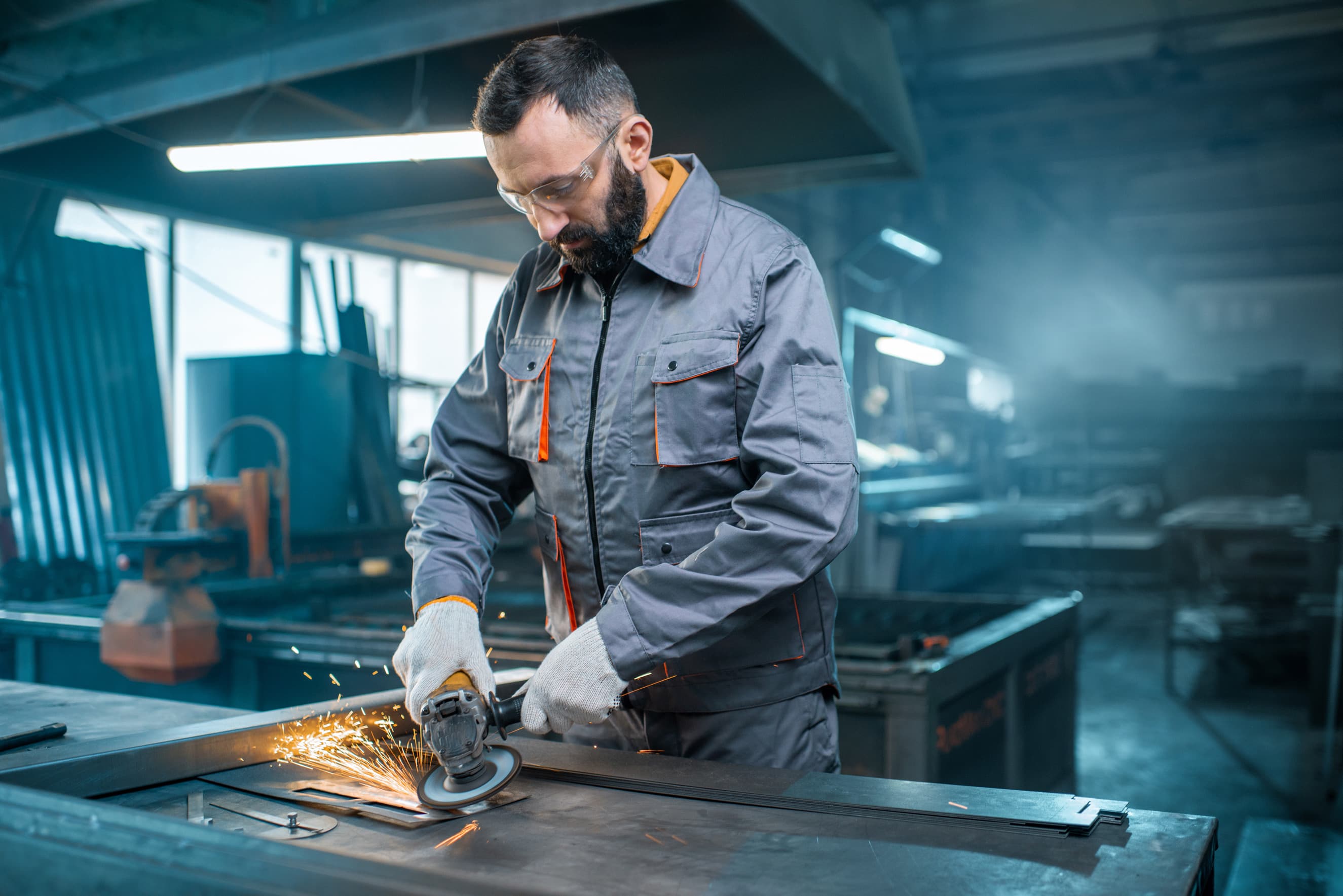 Hombre trabajando en un taller con una amoladora angular, generando chispas mientras corta metal