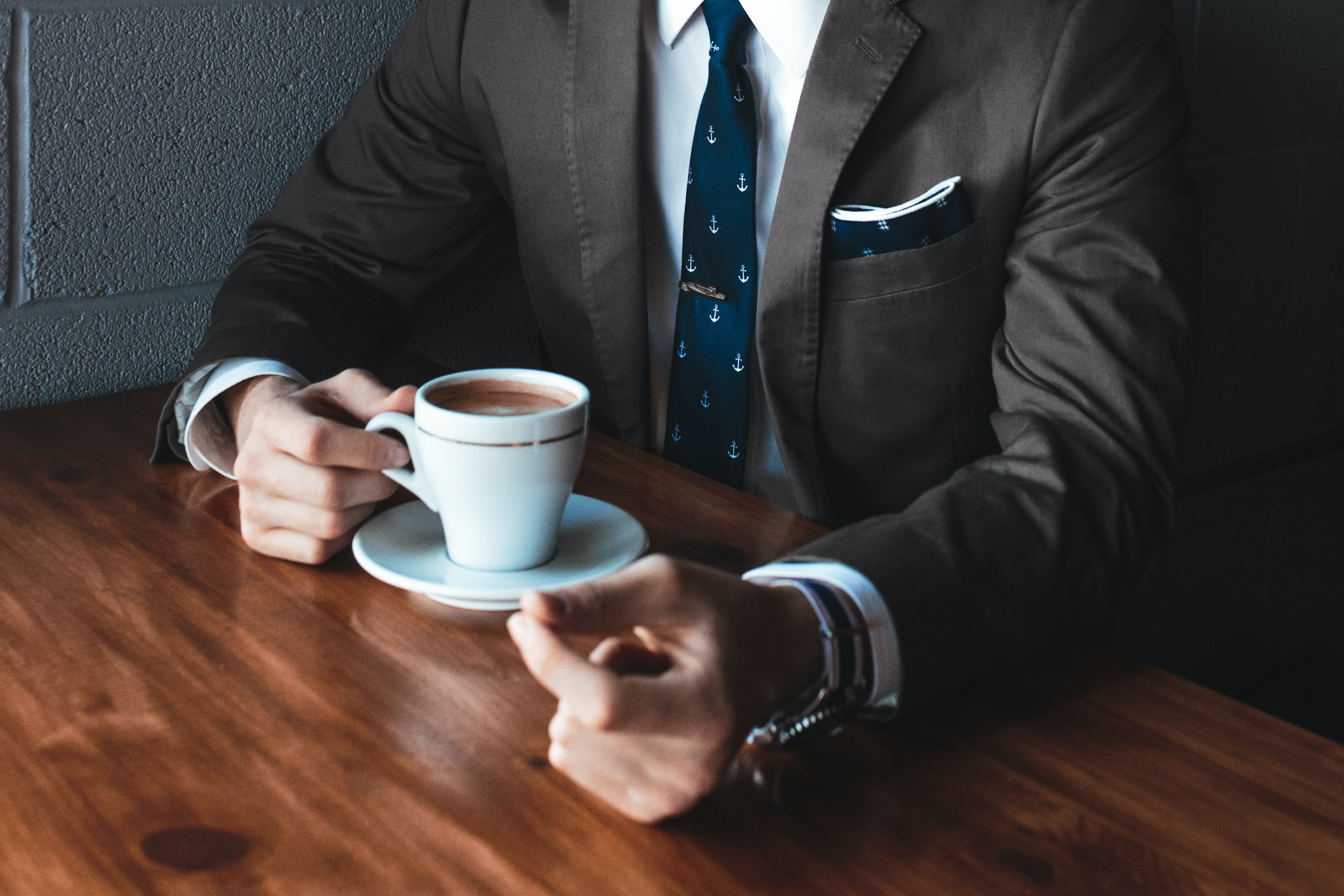 Hombre en traje sosteniendo una taza de café sobre una mesa de madera.