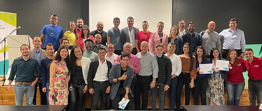 Grupo numeroso de personas sonriendo y posando juntas en un evento, algunas sosteniendo certificados.