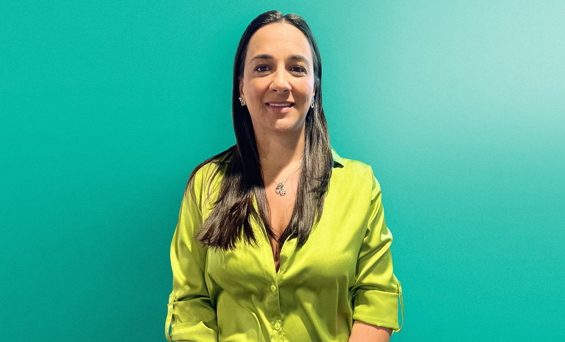 Mujer sonriendo, vestida con una blusa verde brillante, posando frente a una pared verde.