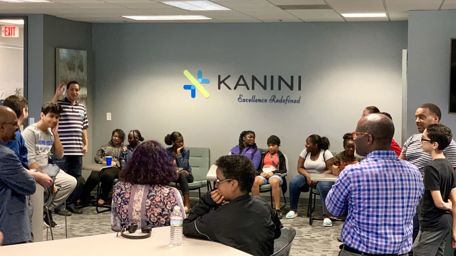 Grupo de personas participando en una reunión informal en las oficinas de Kanini, con su logotipo y eslogan 'Excellence Redefined' visibles en la pared.