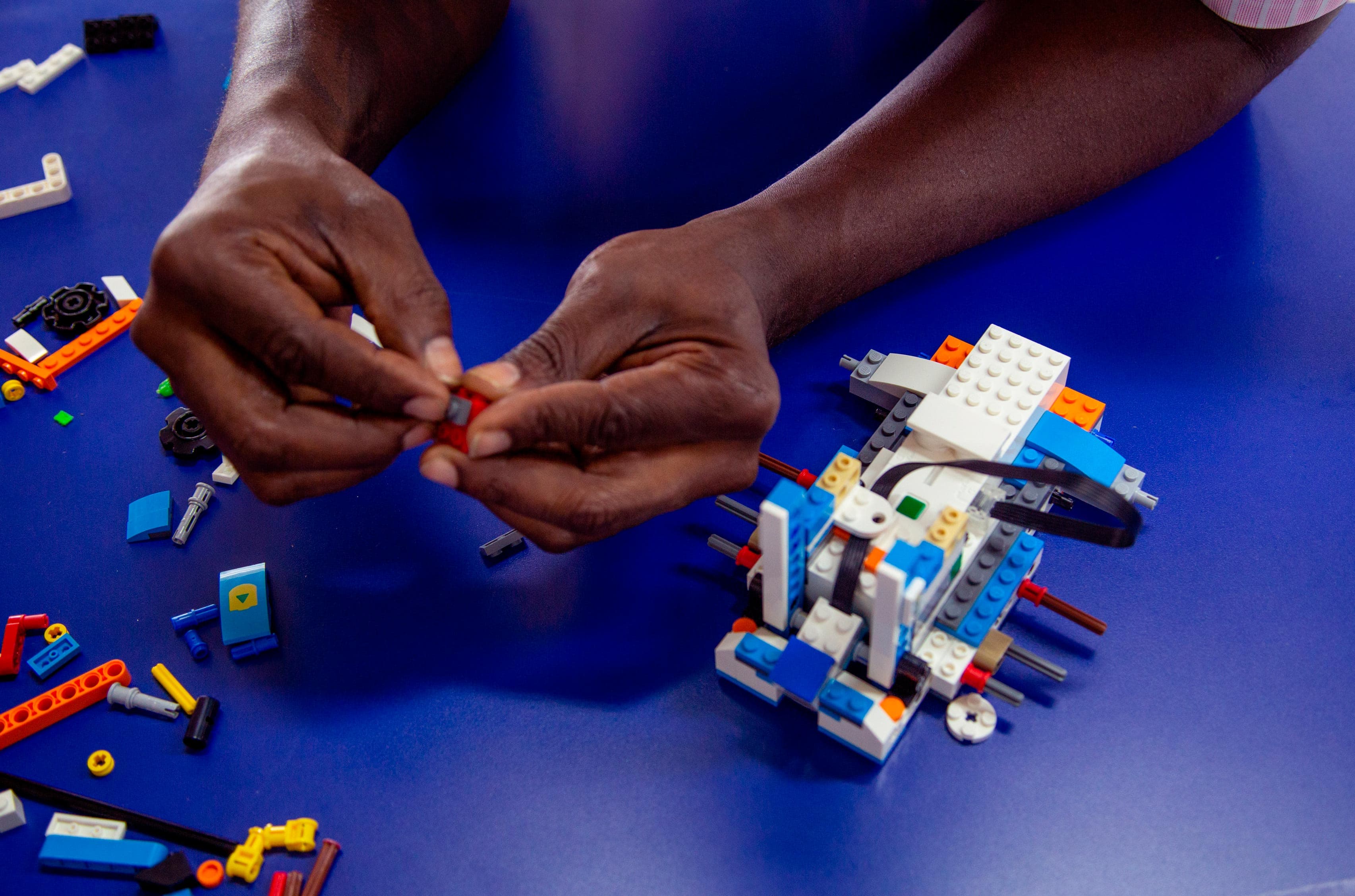 Persona ensamblando piezas de Lego sobre una mesa azul, creando una estructura compleja.