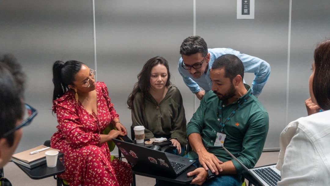 Grupo de personas colaborando alrededor de un portátil, conversando y revisando información juntos.