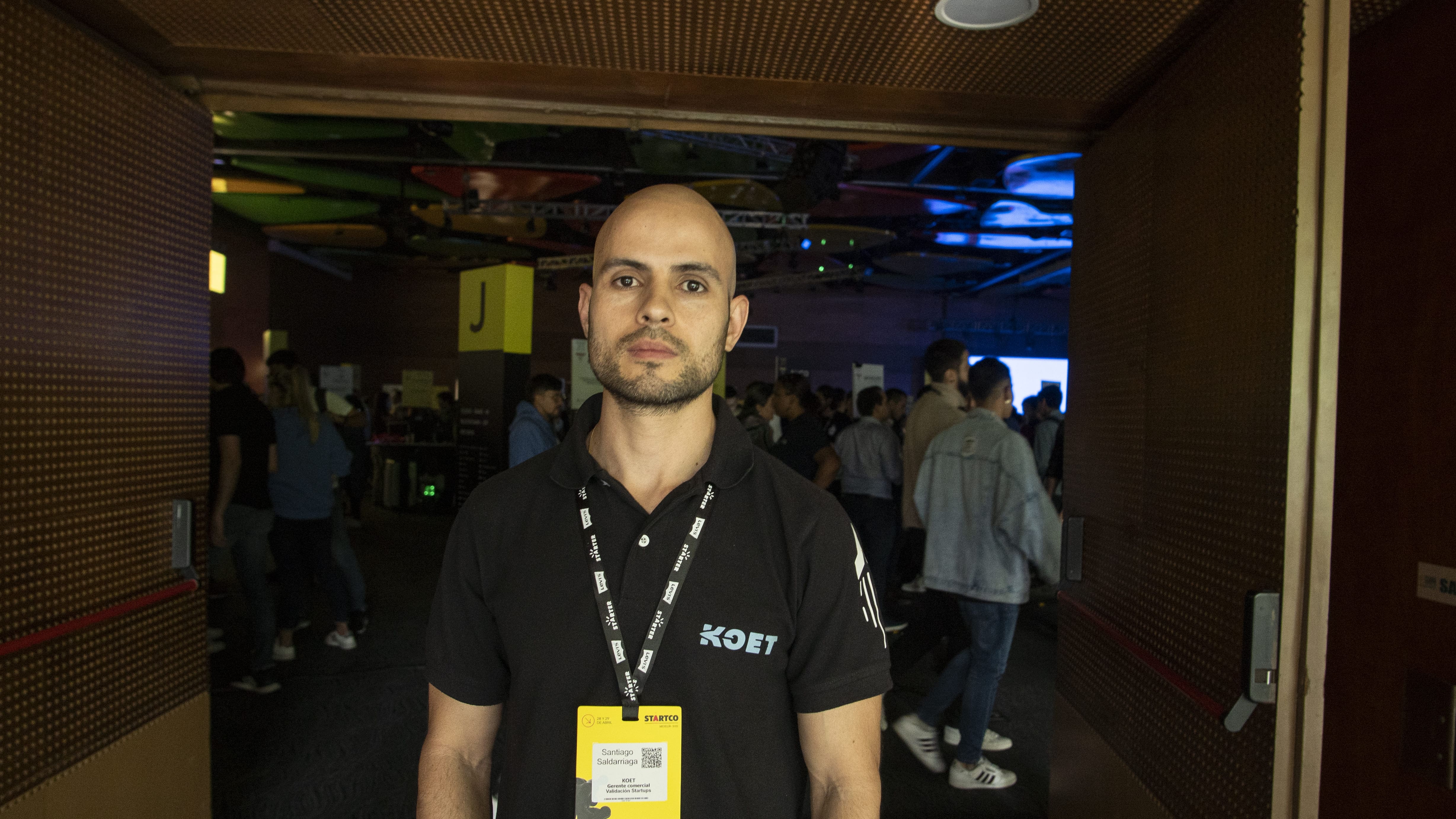 Persona en primer plano en un evento concurrido con iluminación colorida y un ambiente vibrante.