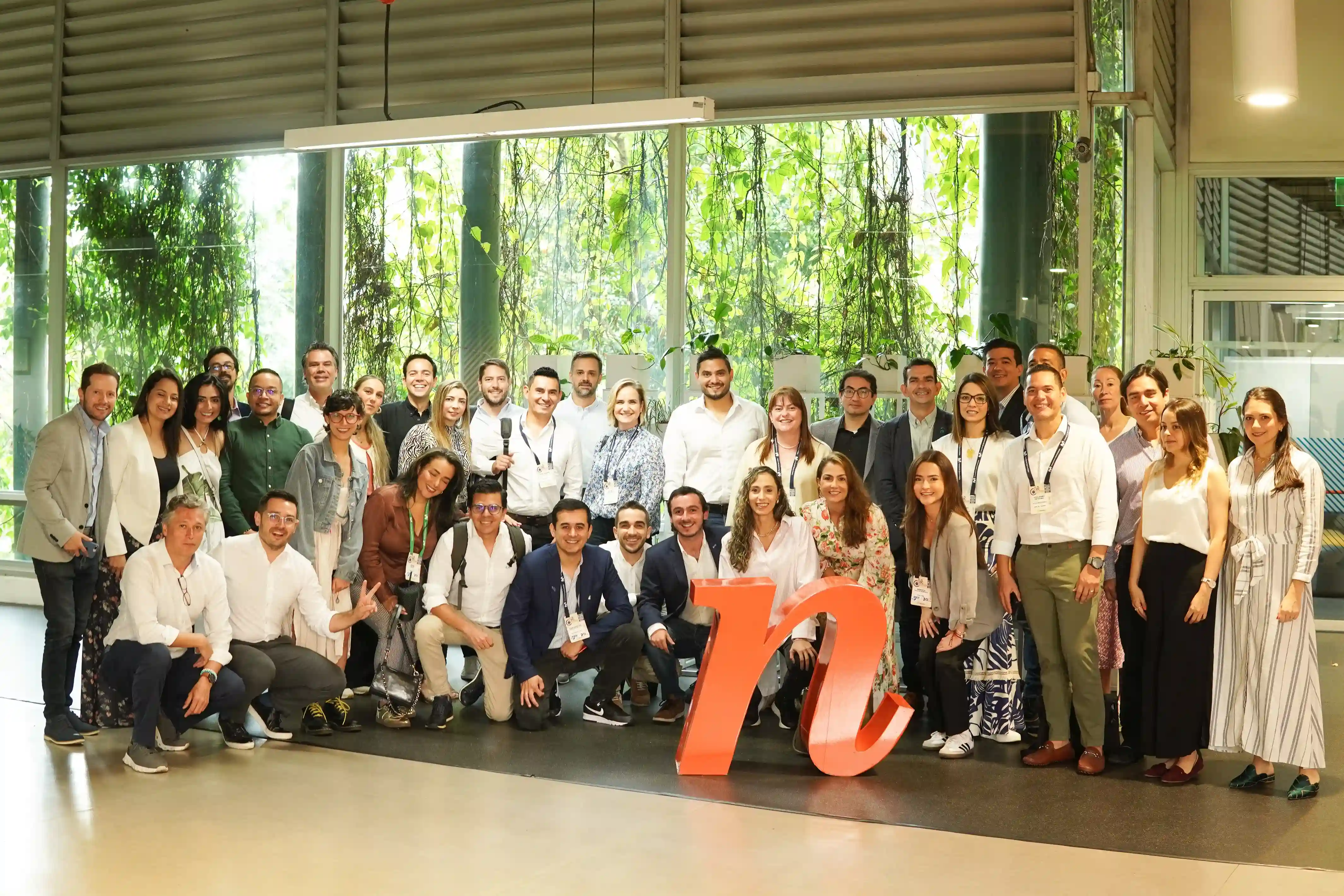 Grupo de personas en la sede de Ruta N posando para una foto grupal junto a un logo naranja, representando la comunidad de innovación y colaboración en Medellín.